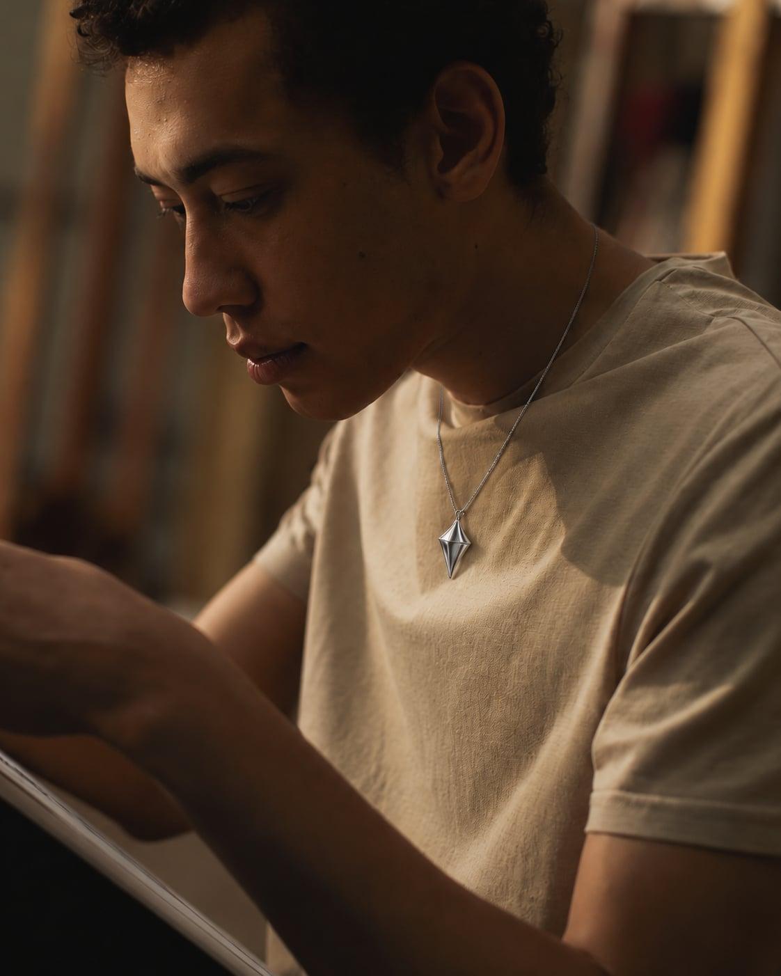 Photographic jewelry styling composite showing Glimmer on a fine silver chain over an artist’s cotton T-shirt