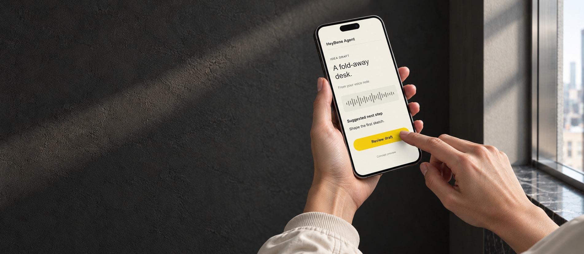 Generated companion phone-use photograph: hands with light stone jacket cuffs review an illustrative HeyBene Agent idea draft beside the same textured wall, metal window reveal and dark stone sill; the screen is a concept preview